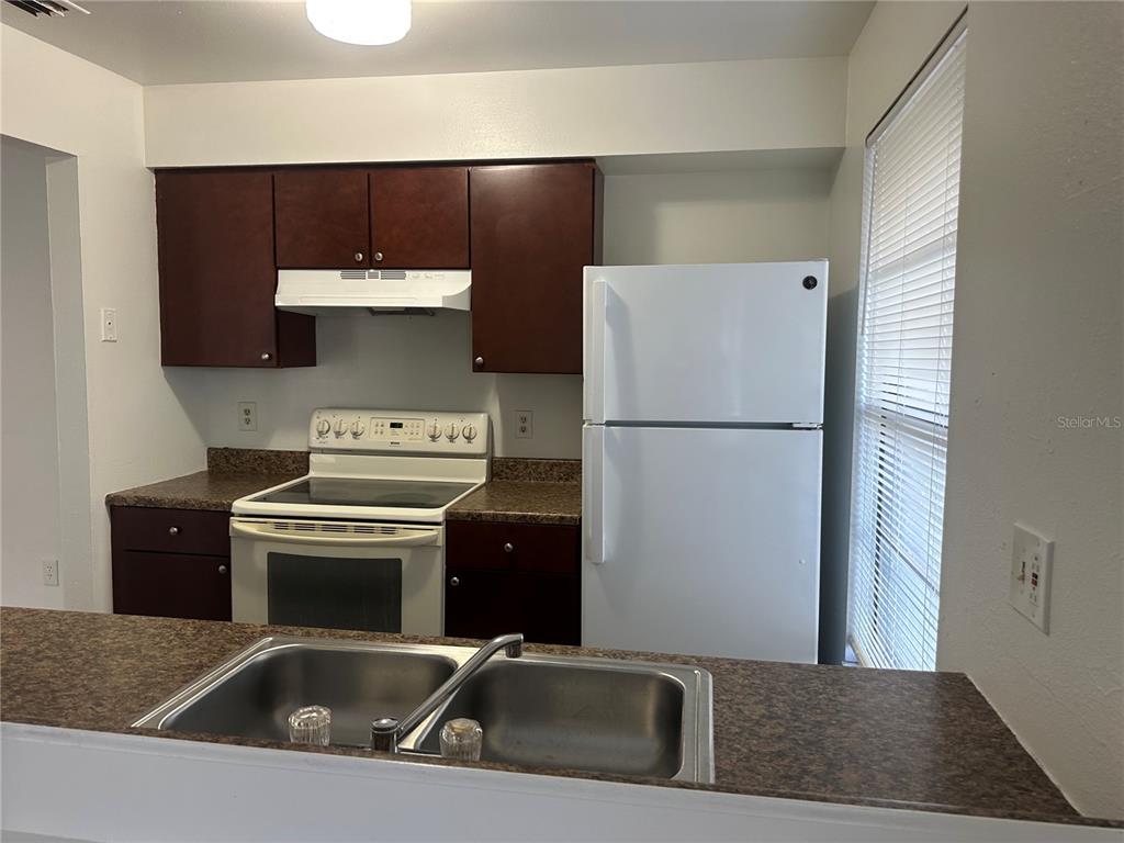 A kitchen features dark wood cabinets, white appliances, and a double-basin sink on the counter — 8428 CAMDEN STREET UNIT C, TAMPA, FL