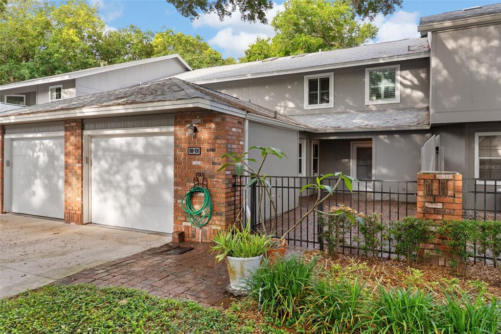 A two-story townhouse exterior features a brick-faced garage, a gated courtyard, and gray siding — 618 MAPLE OAK CIRCLE UNIT 108, ALTAMONTE SPRINGS, FL