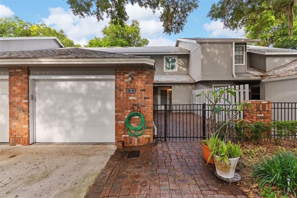 A brick-fronted townhouse features a white garage door, a gated brick courtyard, and gray siding — 618 MAPLE OAK CIRCLE UNIT 108, ALTAMONTE SPRINGS, FL