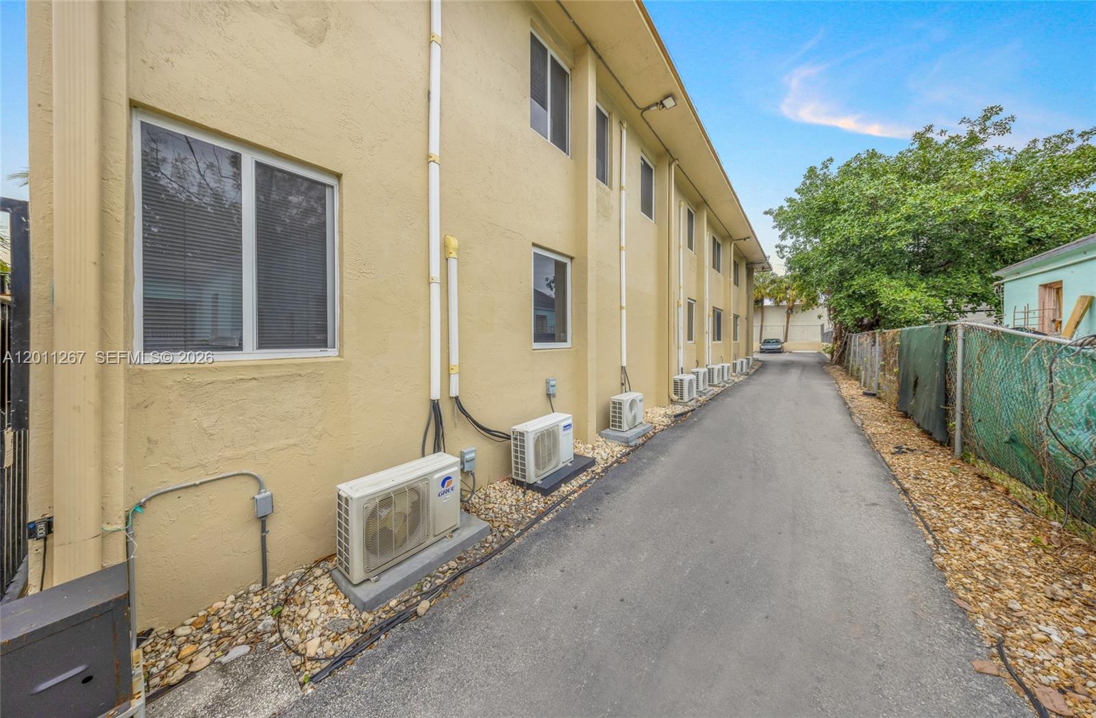 The exterior of a multi-story building features several wall-mounted air conditioning units along a paved alley — 1 NE 78th St, Miami FL 33138, MIAMI, FL