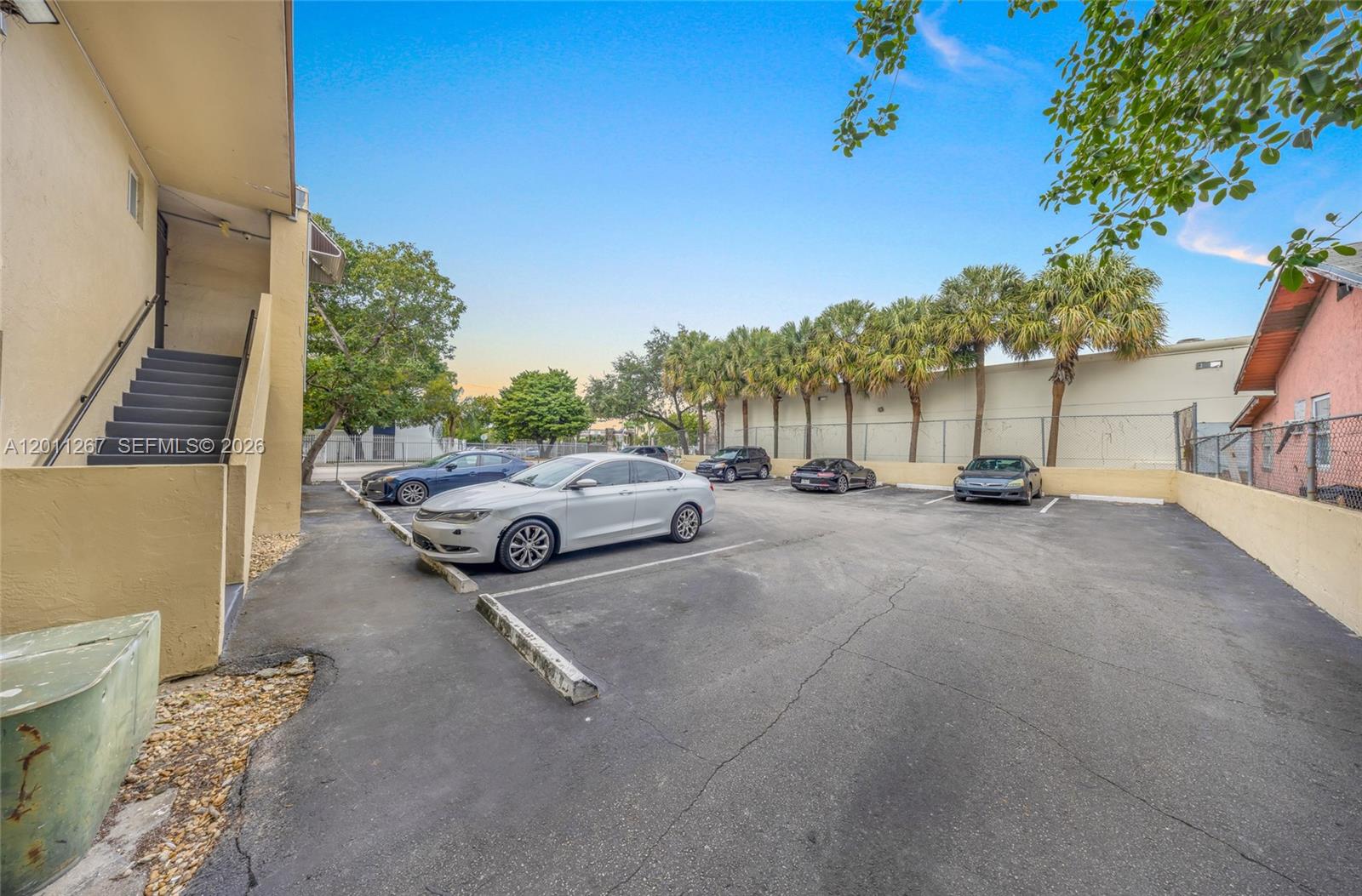 An outdoor parking lot features several parked cars next to a building with stairs — 1 NE 78th St, Miami FL 33138, MIAMI, FL