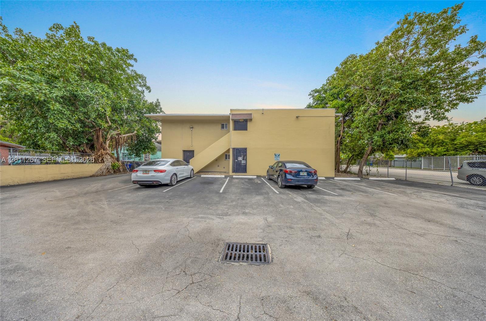 The exterior of a two-story yellow building features a parking lot with two parked cars — 1 NE 78th St, Miami FL 33138, MIAMI, FL