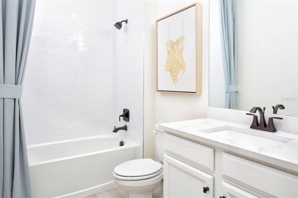 A bathroom features a white subway tile shower, a vanity with a marble countertop, and toilet — 11811 STARBRIGHT PATH, VENICE, FL