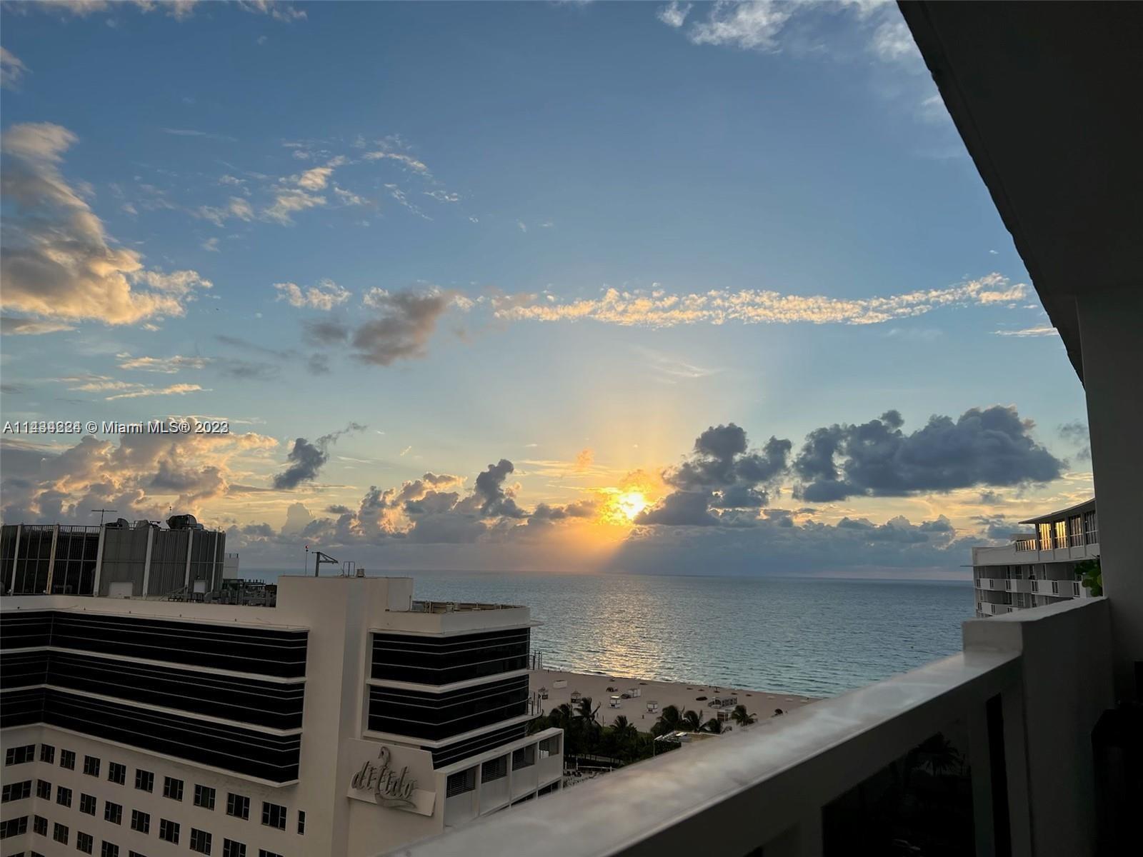 A balcony view overlooks a beach, the ocean, and nearby buildings during a sunset — 100 Lincoln Rd # 1612, Miami Beach FL 33139, MIAMI BEACH, FL