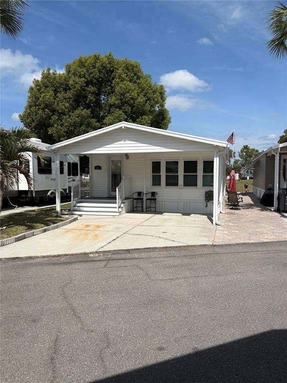 A white manufactured home features a covered front porch, concrete driveway, and adjacent paved patio — 9000 US HIGHWAY 192 UNIT 894, CLERMONT, FL