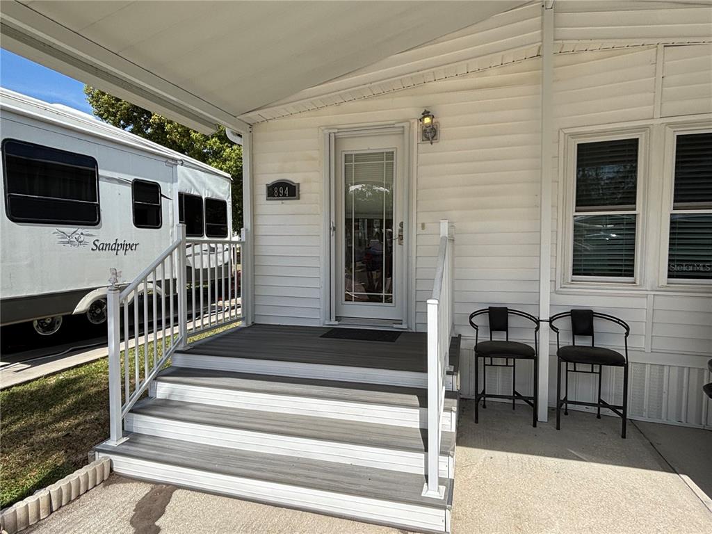 A white mobile home features a gray-stepped porch, a glass-paneled door, and two metal chairs — 9000 US HIGHWAY 192 UNIT 894, CLERMONT, FL