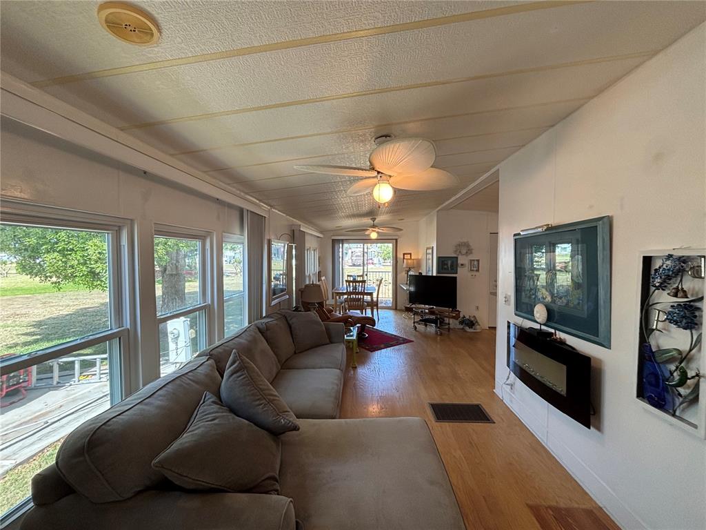 A living room with a sectional sofa, wood flooring, ceiling fans, and a wall-mounted fireplace — 9000 US HIGHWAY 192 UNIT 894, CLERMONT, FL