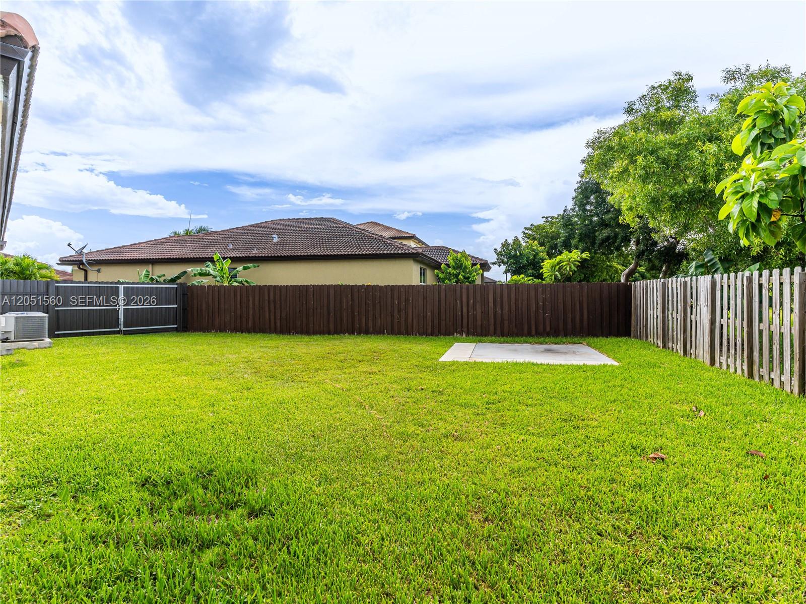 A grassy backyard features a wooden privacy fence, a concrete pad, and a metal gate — 28381 SW 128th Pl, Homestead FL 33033, HOMESTEAD, FL