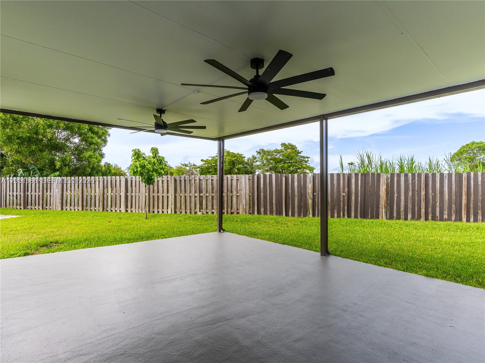 A covered patio features two ceiling fans, a concrete floor, and a wooden fence — 28381 SW 128th Pl, Homestead FL 33033, HOMESTEAD, FL