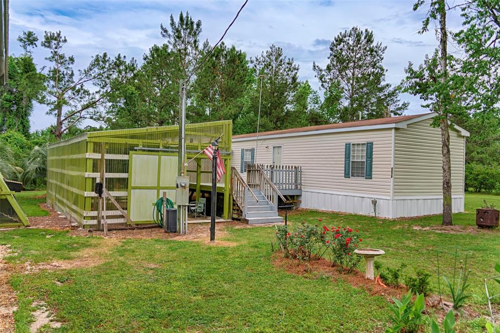 A mobile home with a green attached greenhouse and wooden stairs in a grassy yard — 7776 SE 113TH COURT, JASPER, FL