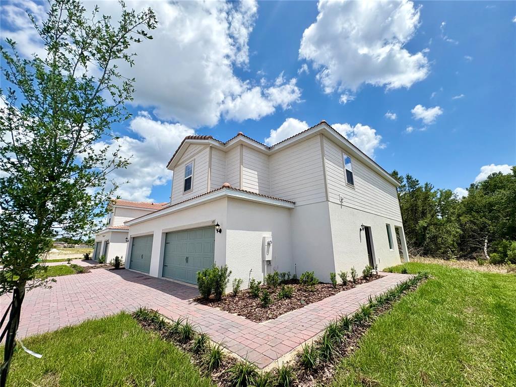 A two-story house with a light-colored exterior, two garage doors, and a brick paver driveway — 571 BAY LEAF DRIVE, POINCIANA, FL