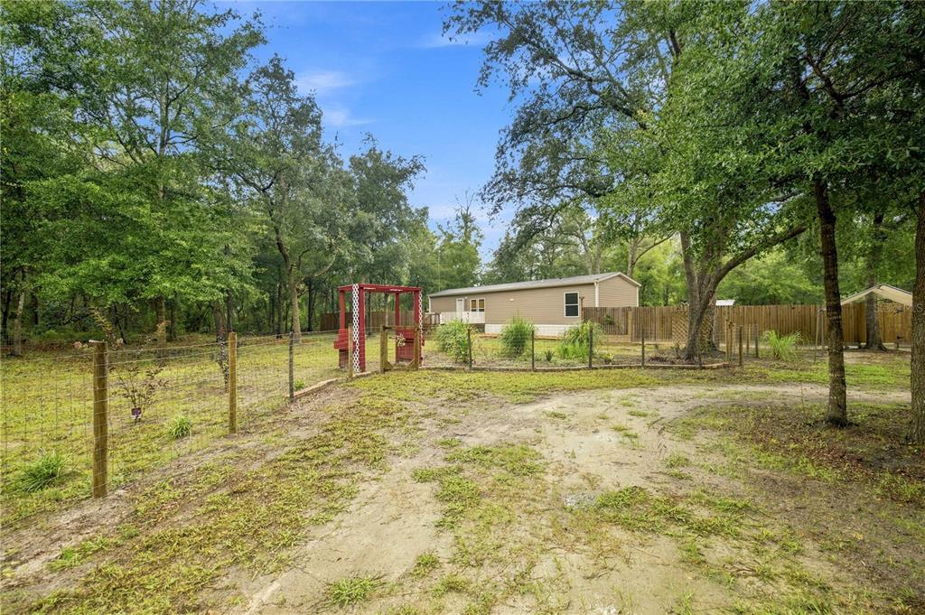 A single-story manufactured home sits behind a fenced yard with a red swing set — 11821 SE 82ND STREET, MORRISTON, FL