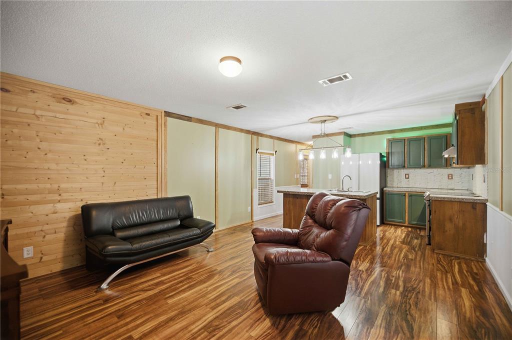 An open-concept living room and kitchen featuring wood-paneled walls, wood flooring, and green cabinetry — 11821 SE 82ND STREET, MORRISTON, FL