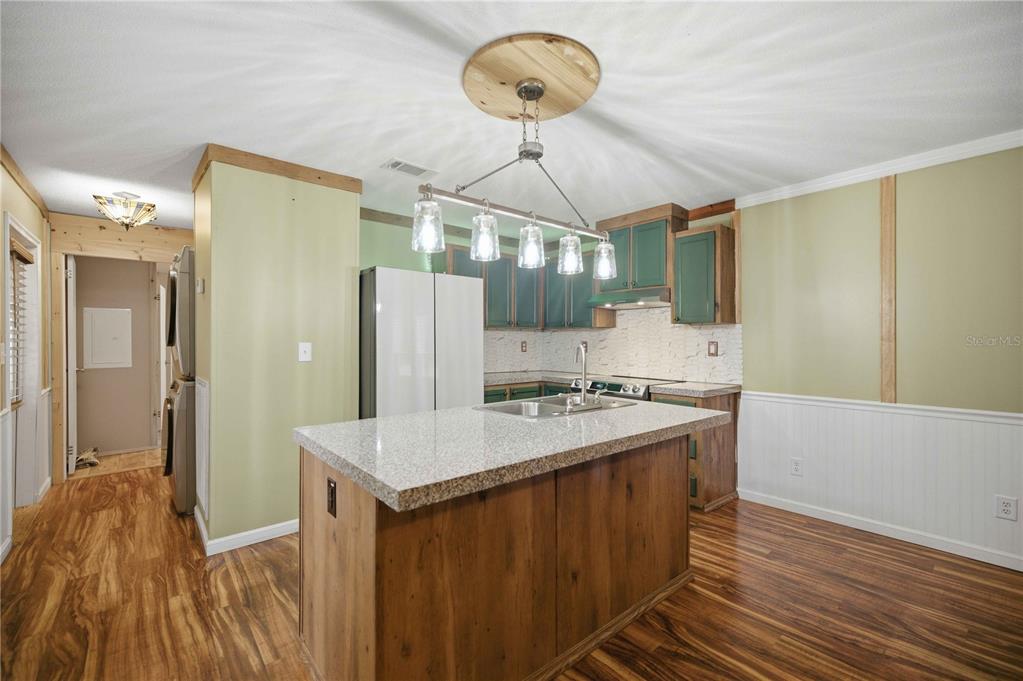 A kitchen features a central island with a granite countertop, green cabinets, and wood flooring — 11821 SE 82ND STREET, MORRISTON, FL