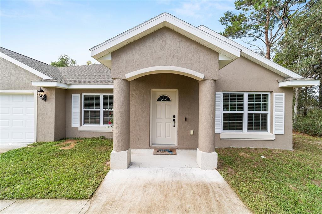 A single-story house with a beige stucco exterior, a covered entryway, and a white door — 15792 SW 55TH AVENUE ROAD, OCALA, FL