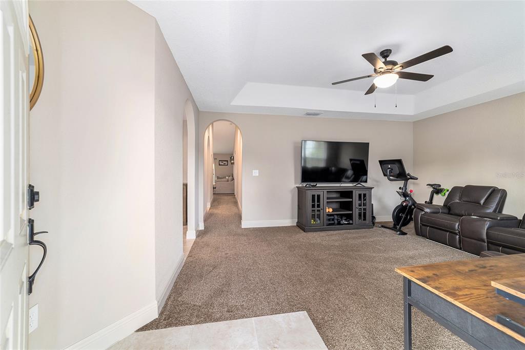A carpeted living room features a tray ceiling, a television console, and an exercise bike — 15792 SW 55TH AVENUE ROAD, OCALA, FL