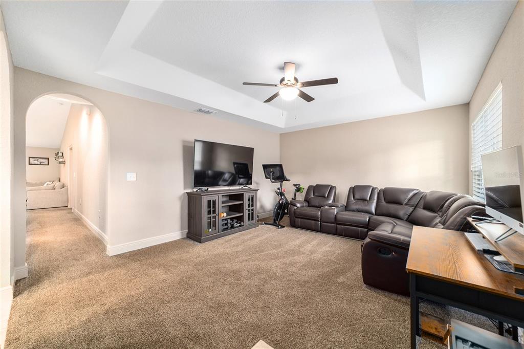 A living room features a tray ceiling, brown carpet, a sectional sofa, and a television console — 15792 SW 55TH AVENUE ROAD, OCALA, FL