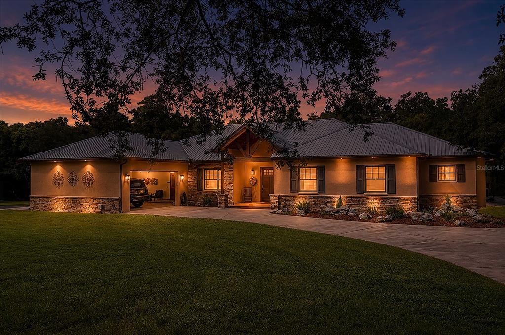 A single-story house with a stone facade, metal roof, and attached garage at dusk — 1617 HORSESHOE CREEK ROAD, DAVENPORT, FL
