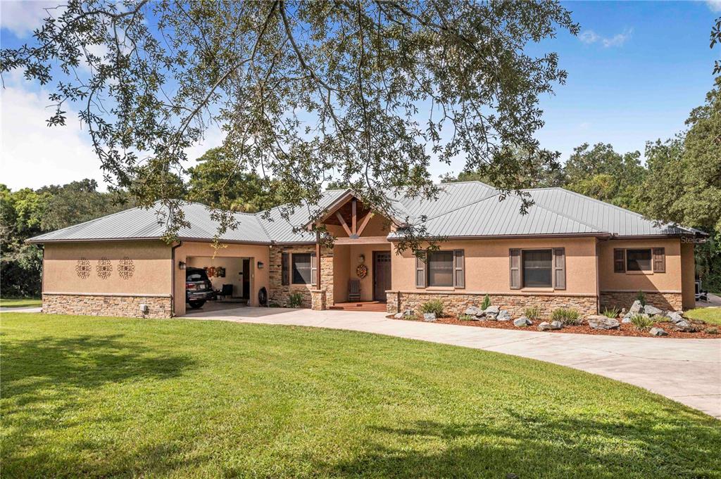 A single-story house with a metal roof, stucco and stone exterior, and an attached garage — 1617 HORSESHOE CREEK ROAD, DAVENPORT, FL
