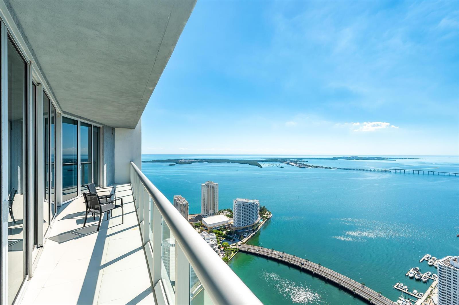 A high-rise balcony with chairs overlooks a bay, a bridge, and city buildings — 495 Brickell Avenue # 5605, Miami FL 33131, MIAMI, FL