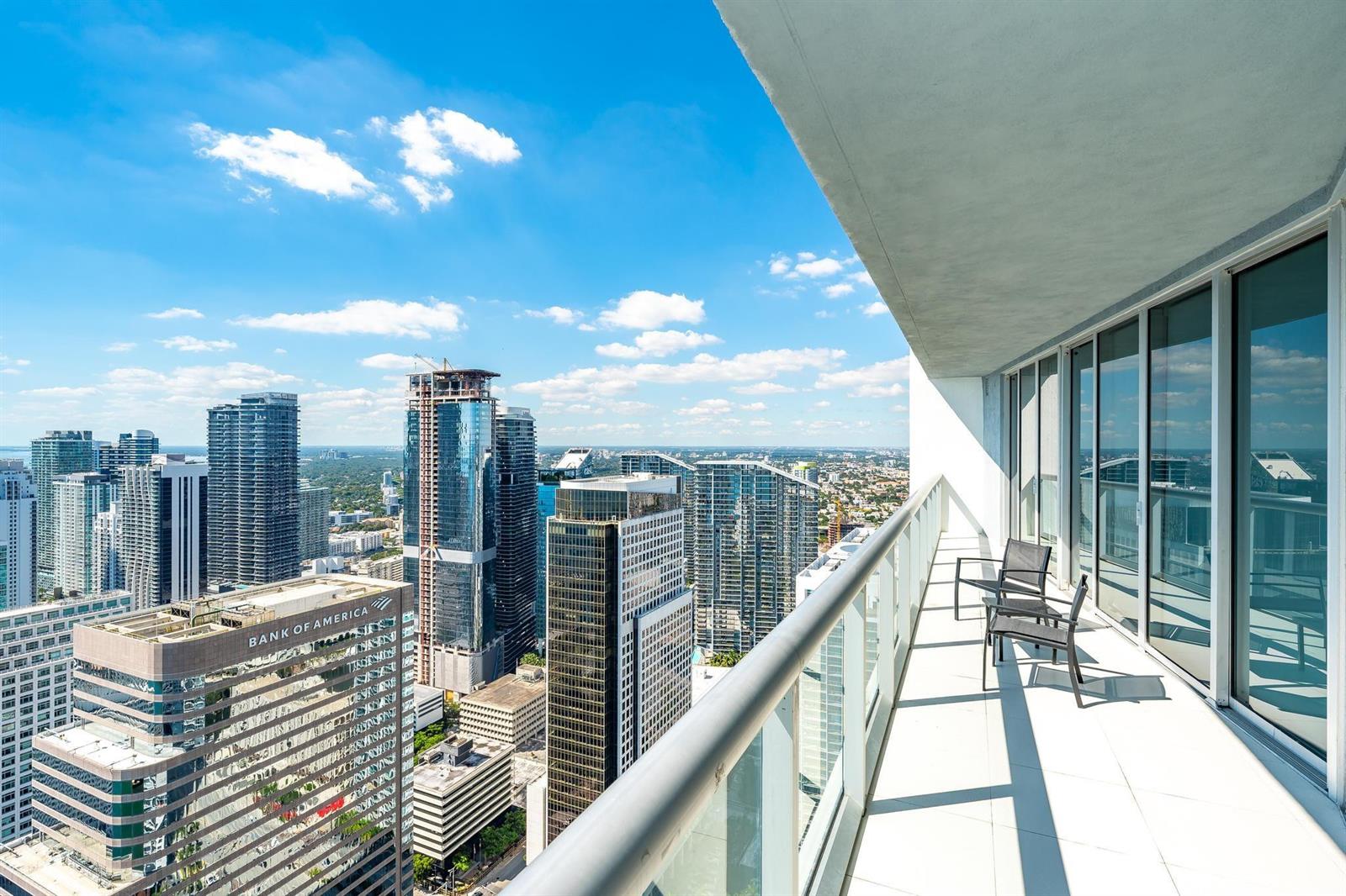 A high-rise balcony with glass railings overlooks a dense city skyline under a blue sky — 495 Brickell Avenue # 5605, Miami FL 33131, MIAMI, FL