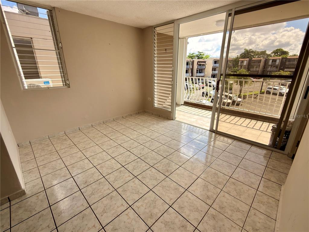 An empty room with beige tile flooring, a side window, and a sliding glass balcony door — 2 CALLE UNIT 227, TRUJILLO ALTO, PR