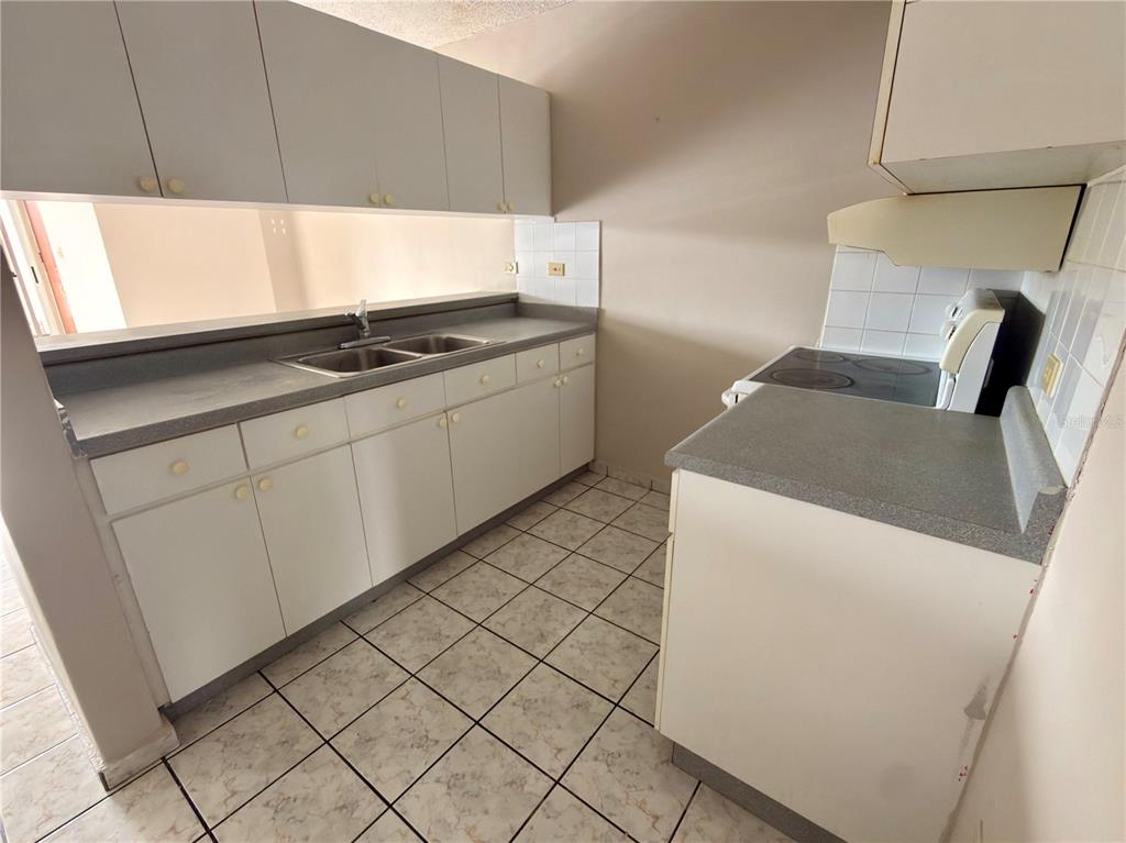 A kitchen features white cabinets, a double sink, a stove, and light-colored tiled flooring — 2 CALLE UNIT 227, TRUJILLO ALTO, PR