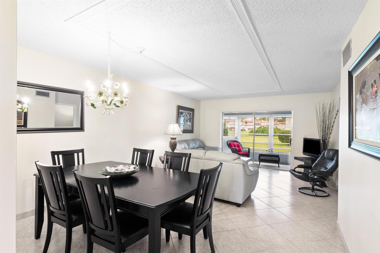 A dining area with a dark wood table and chairs opens into a living room — 3 Abbey Lane # 102, Delray Beach FL 33446, DELRAY BEACH, FL