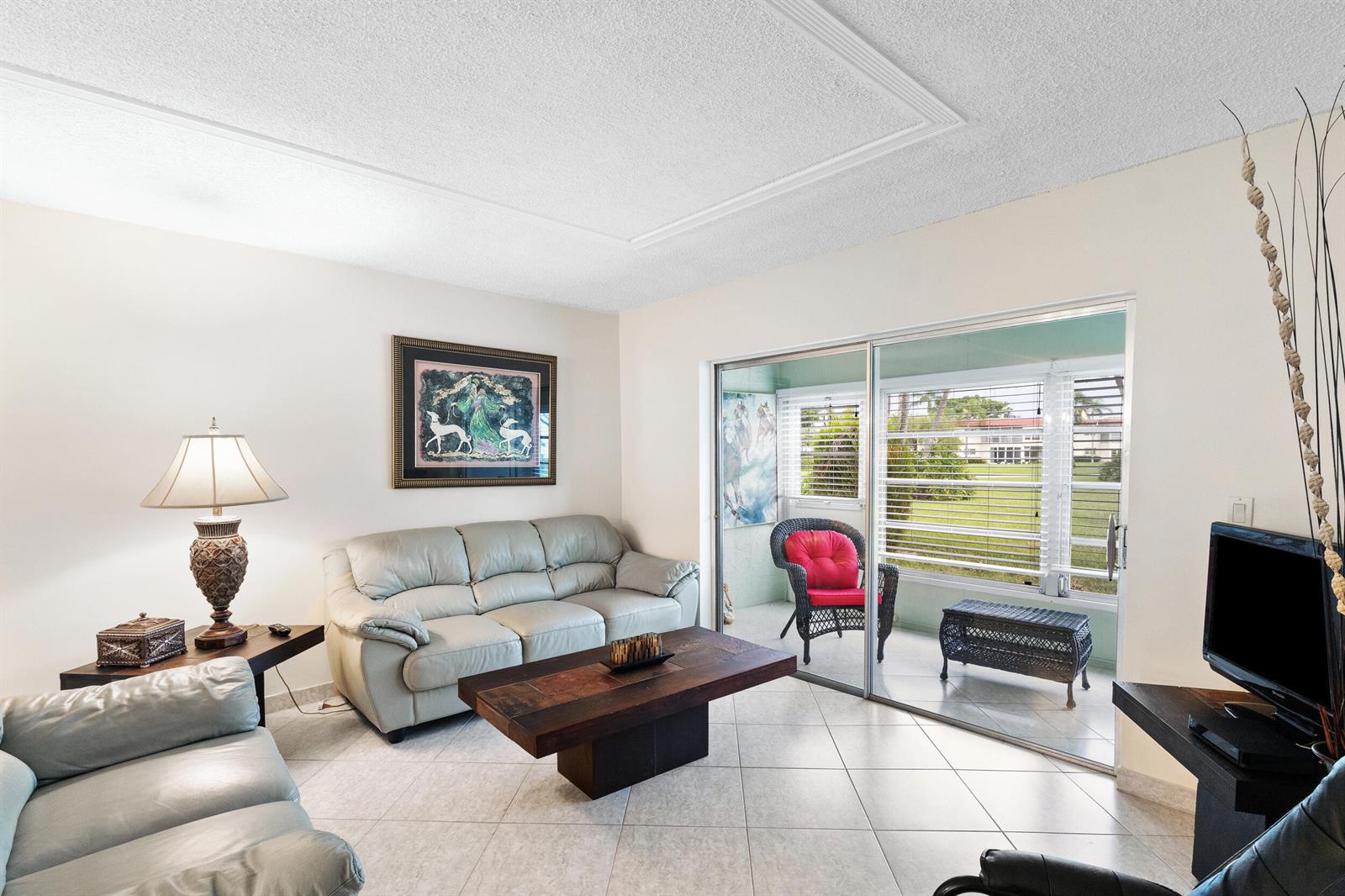 A living room with light tile floors, leather sofas, a wooden coffee table, and a patio — 3 Abbey Lane # 102, Delray Beach FL 33446, DELRAY BEACH, FL