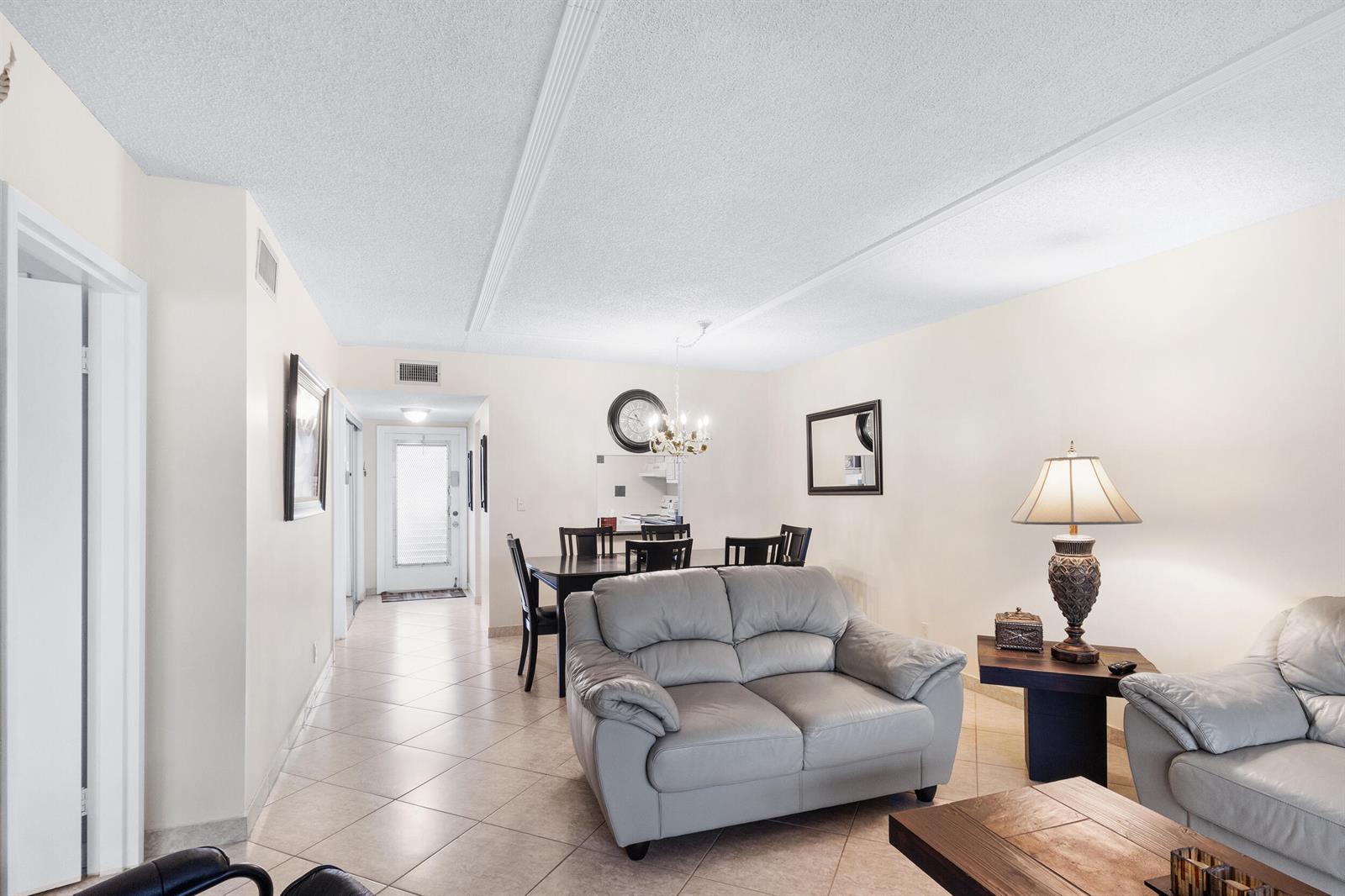 A living and dining area with tile floors, light-colored walls, and two leather sofas — 3 Abbey Lane # 102, Delray Beach FL 33446, DELRAY BEACH, FL