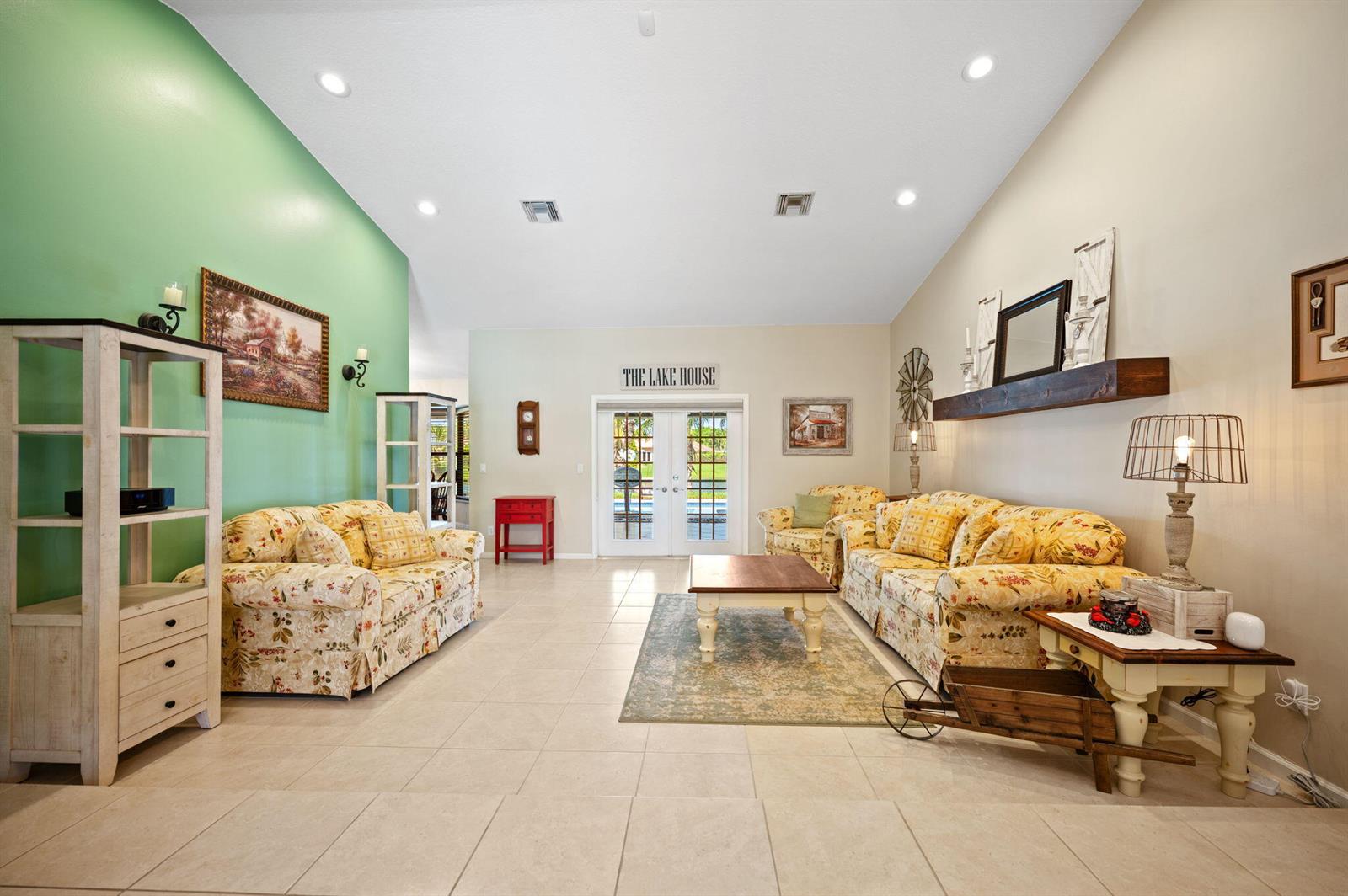 A living room with floral sofas, tile floors, a green accent wall, and French doors — 5531 Hawkes Bluff Avenue, Davie FL 33331, DAVIE, FL