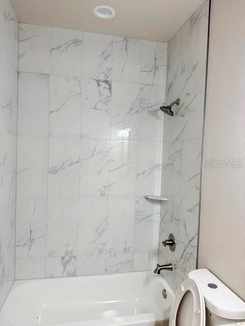 A bathroom features a white bathtub with marble-look tile walls and a shower head — 29 SLUMBER PATH UNIT A, PALM COAST, FL