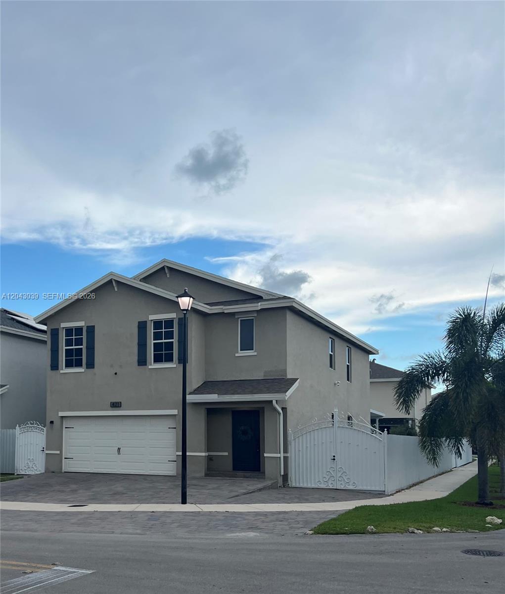 A two-story suburban house features a gray stucco exterior, a white garage, and gated side yards — 421 NE 6th Ct, Florida City FL 33034, FLORIDA CITY, FL