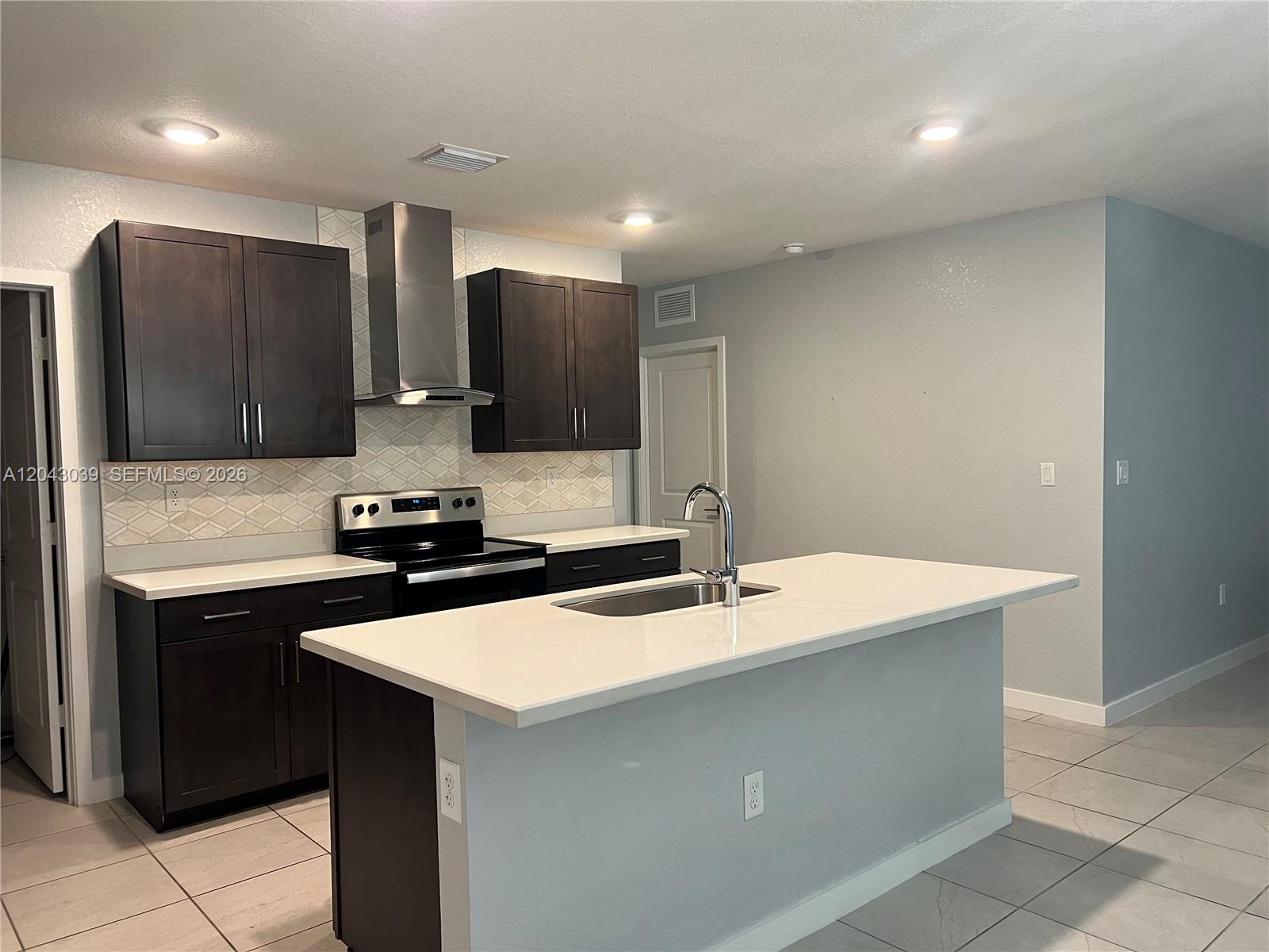 A kitchen features dark wood cabinets, white countertops, a central island, and stainless steel appliances — 421 NE 6th Ct, Florida City FL 33034, FLORIDA CITY, FL