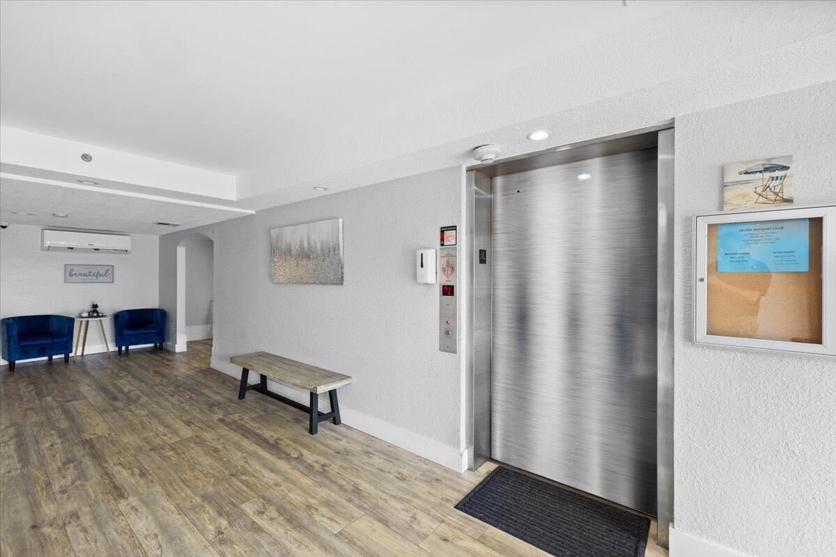 An elevator lobby features wood-look flooring, a wooden bench, two blue chairs, and a bulletin board — 2255 Lindell Boulevard # 4401, Delray Beach FL 33444, DELRAY BEACH, FL