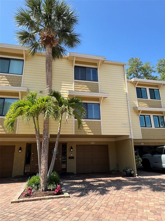 A three-story townhouse exterior features yellow siding, a brick driveway, and a palm tree — 513 HAVEN POINT DRIVE, TREASURE ISLAND, FL