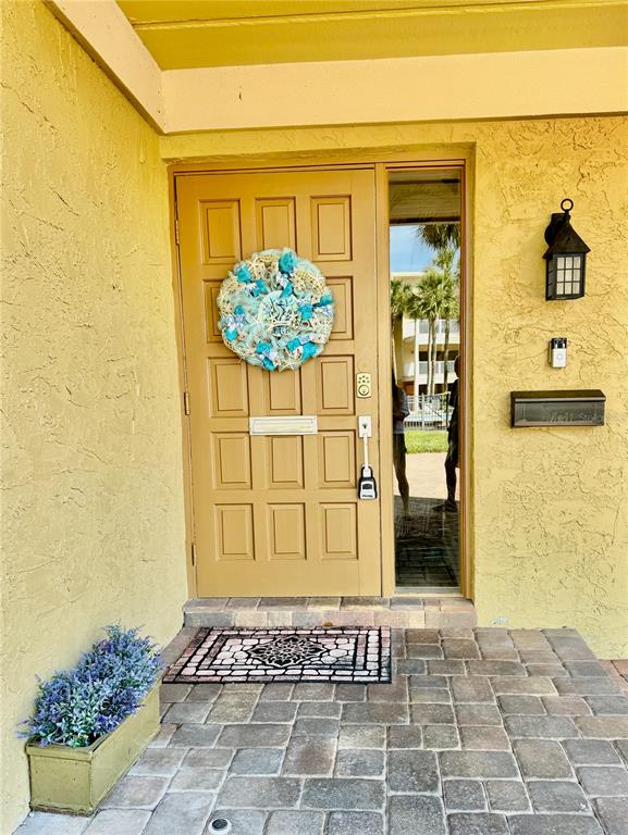 A tan front door with a wreath and a side window opens onto a paved patio — 513 HAVEN POINT DRIVE, TREASURE ISLAND, FL
