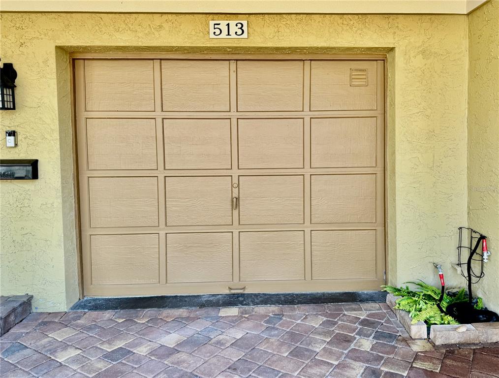 A tan garage door with rectangular panels is set into a yellow stucco exterior wall — 513 HAVEN POINT DRIVE, TREASURE ISLAND, FL