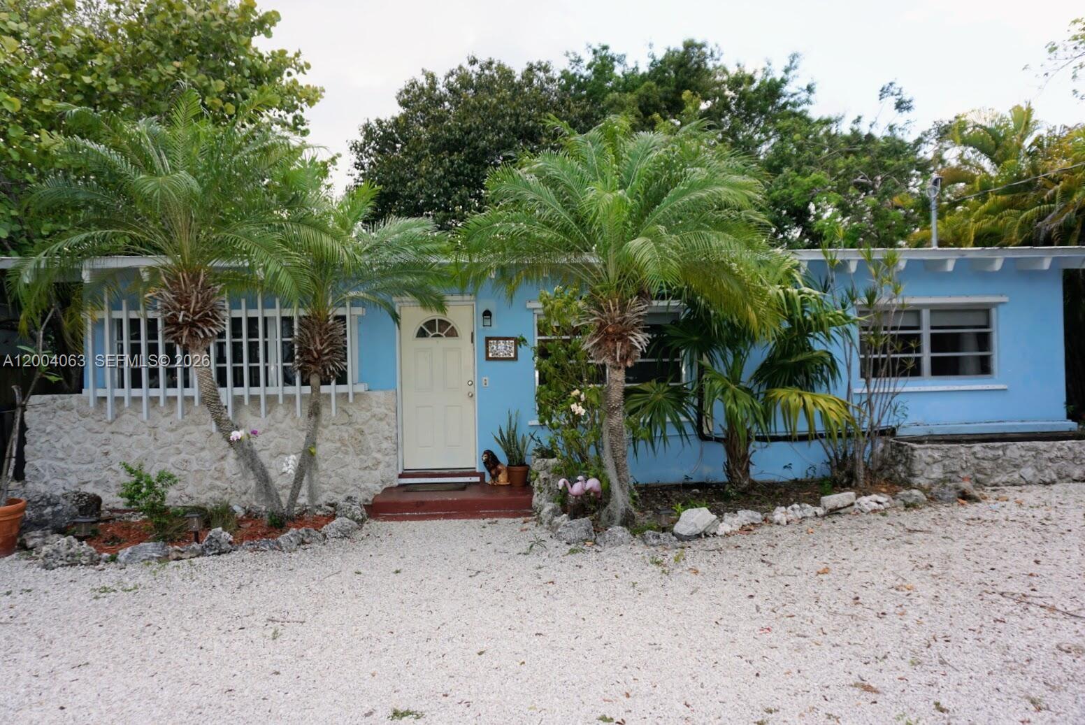 A light blue single-story house features a stone facade, palm trees, and a gravel driveway — 229 2nd Rd, Key Largo FL 33037, KEY LARGO, FL