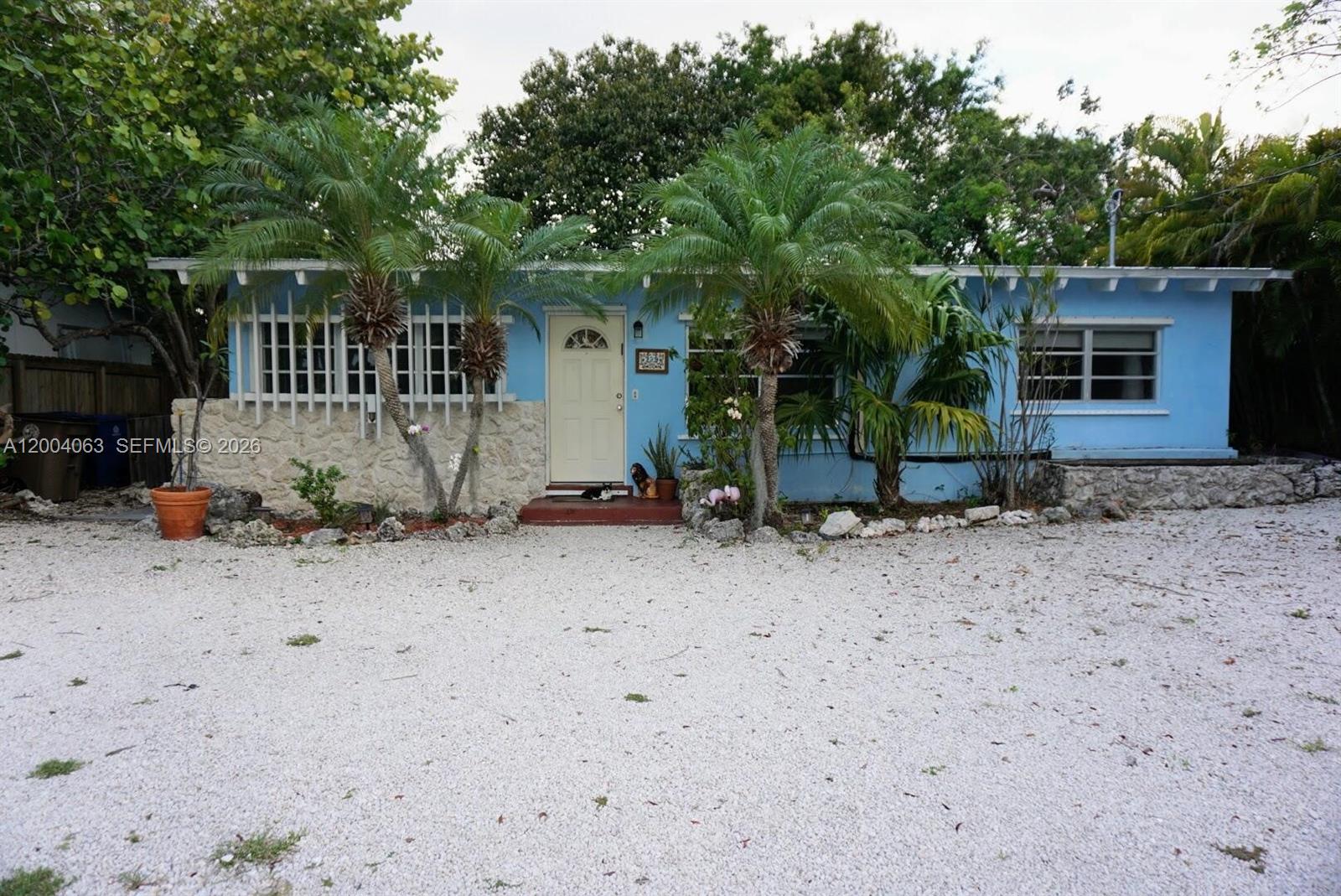 A light blue single-story house features a stone facade, palm trees, and a gravel driveway — 229 2nd Rd, Key Largo FL 33037, KEY LARGO, FL