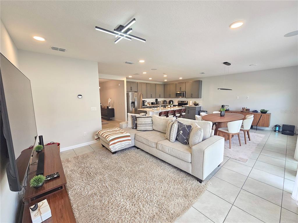 An open-concept living room features a sectional sofa, dining area, and kitchen with gray cabinetry — 3775 KNOTTY PINE STREET, ST CLOUD, FL