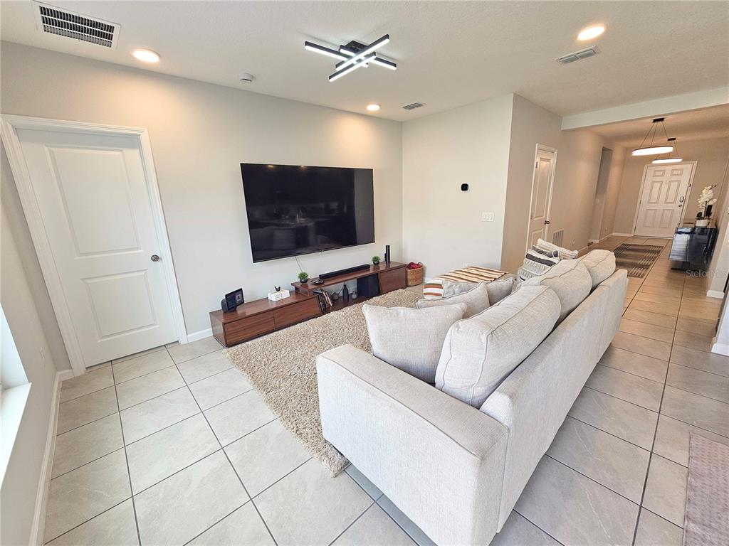 A living room features a large television, a beige sofa, and tile flooring — 3775 KNOTTY PINE STREET, ST CLOUD, FL