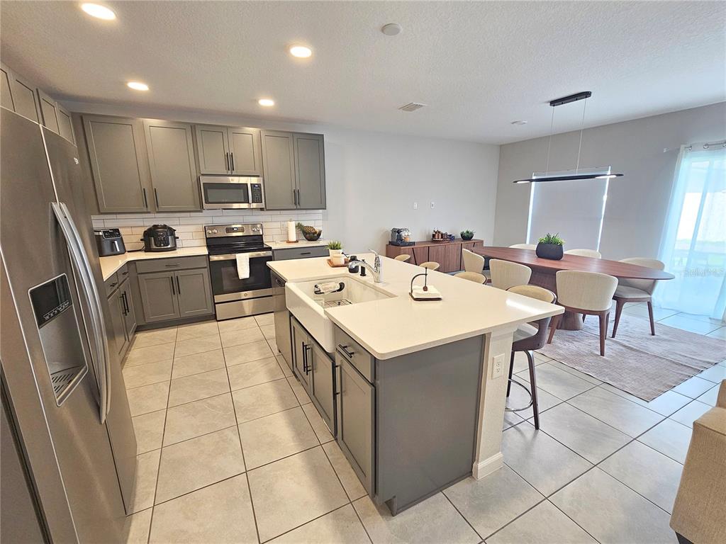 A kitchen with gray cabinets, a white farmhouse sink, and an island with bar seating — 3775 KNOTTY PINE STREET, ST CLOUD, FL