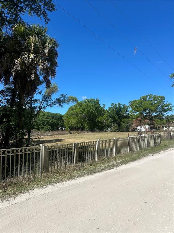 A fenced, grassy vacant lot sits beside a dirt road under a clear blue sky — 1565 CREEK ROAD, WESLEY CHAPEL, FL