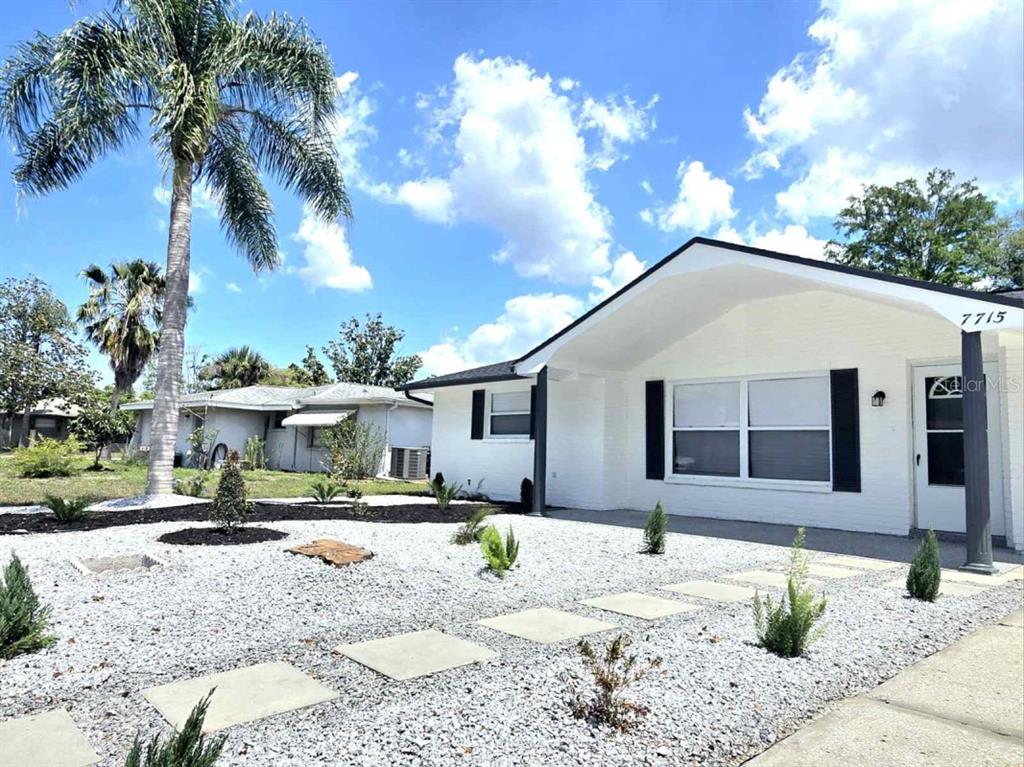 A white single-story house features a gravel front yard with stone pavers and a palm tree — 7715 CHERRYTREE LANE, NEW PORT RICHEY, FL