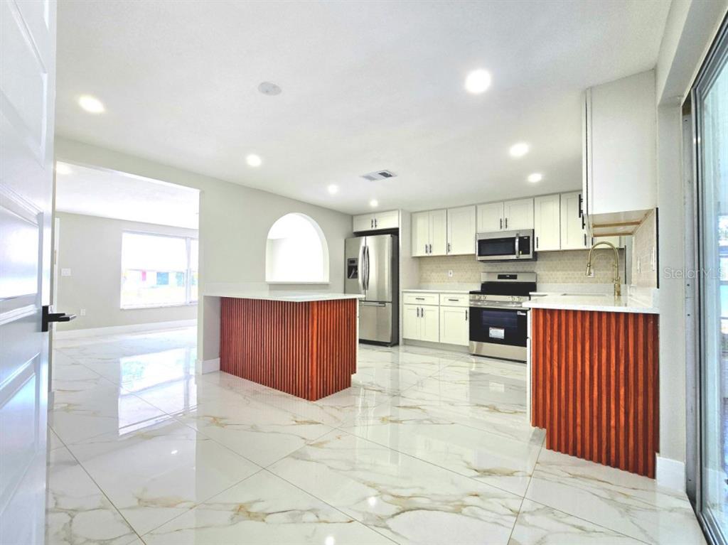 A modern kitchen features white cabinets, stainless steel appliances, and a ribbed wood-paneled island — 7715 CHERRYTREE LANE, NEW PORT RICHEY, FL