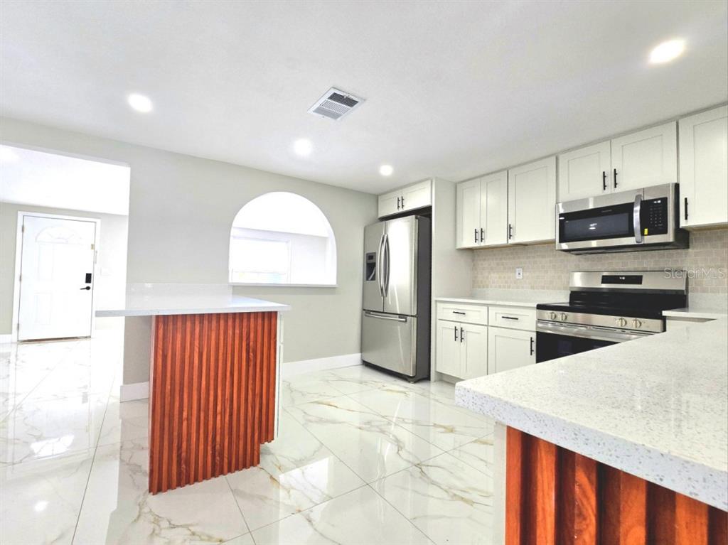A modern kitchen features white cabinetry, stainless steel appliances, and a wood-slatted kitchen island — 7715 CHERRYTREE LANE, NEW PORT RICHEY, FL