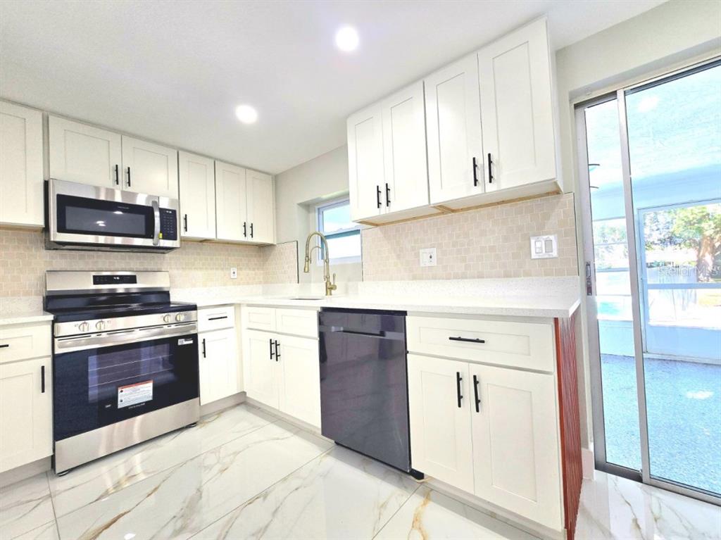 A kitchen features white cabinets, stainless steel appliances, marble-look tile flooring, and a sliding door — 7715 CHERRYTREE LANE, NEW PORT RICHEY, FL