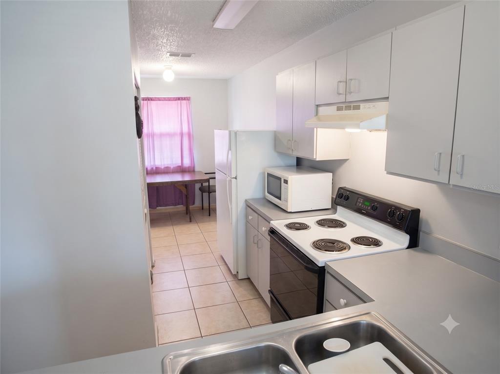A kitchen with white cabinets, a white stove, a microwave, and a dining area beyond — 4975 DAVID AVENUE, SARASOTA, FL