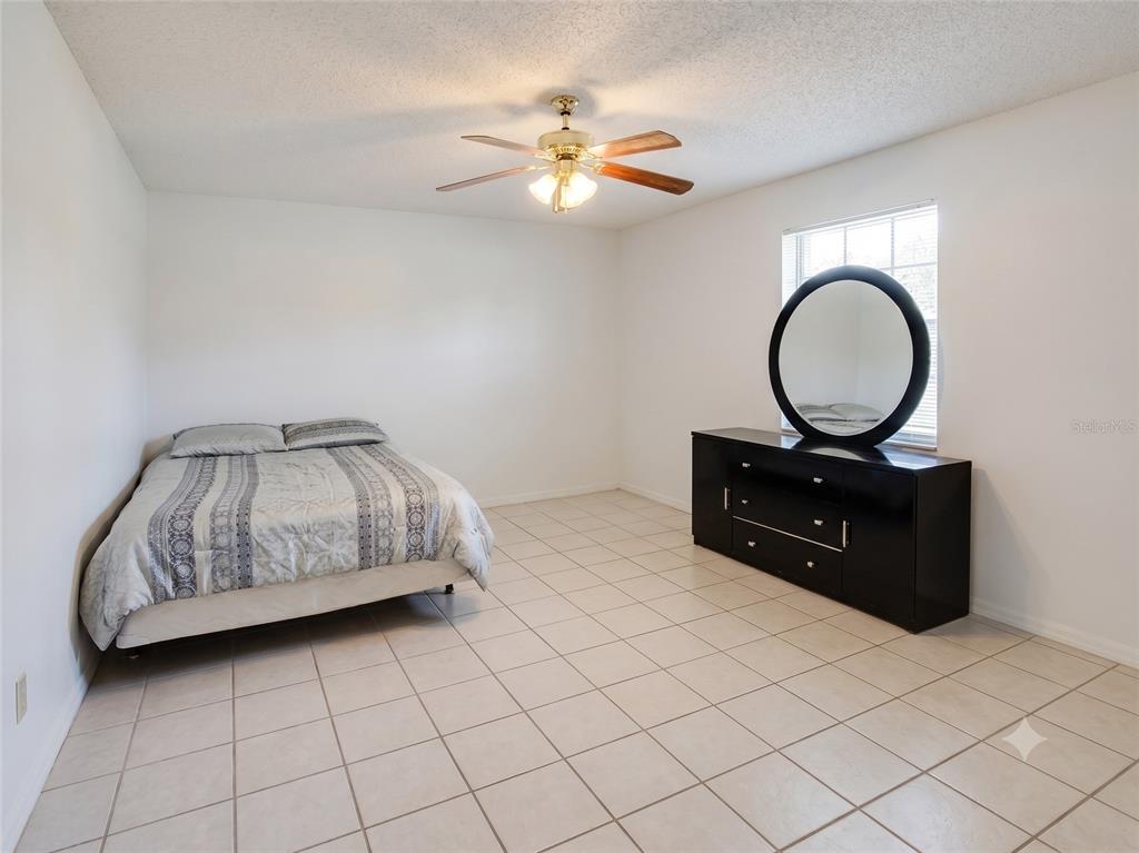 A bedroom features white walls, tile flooring, a bed, and a black dresser with a mirror — 4975 DAVID AVENUE, SARASOTA, FL